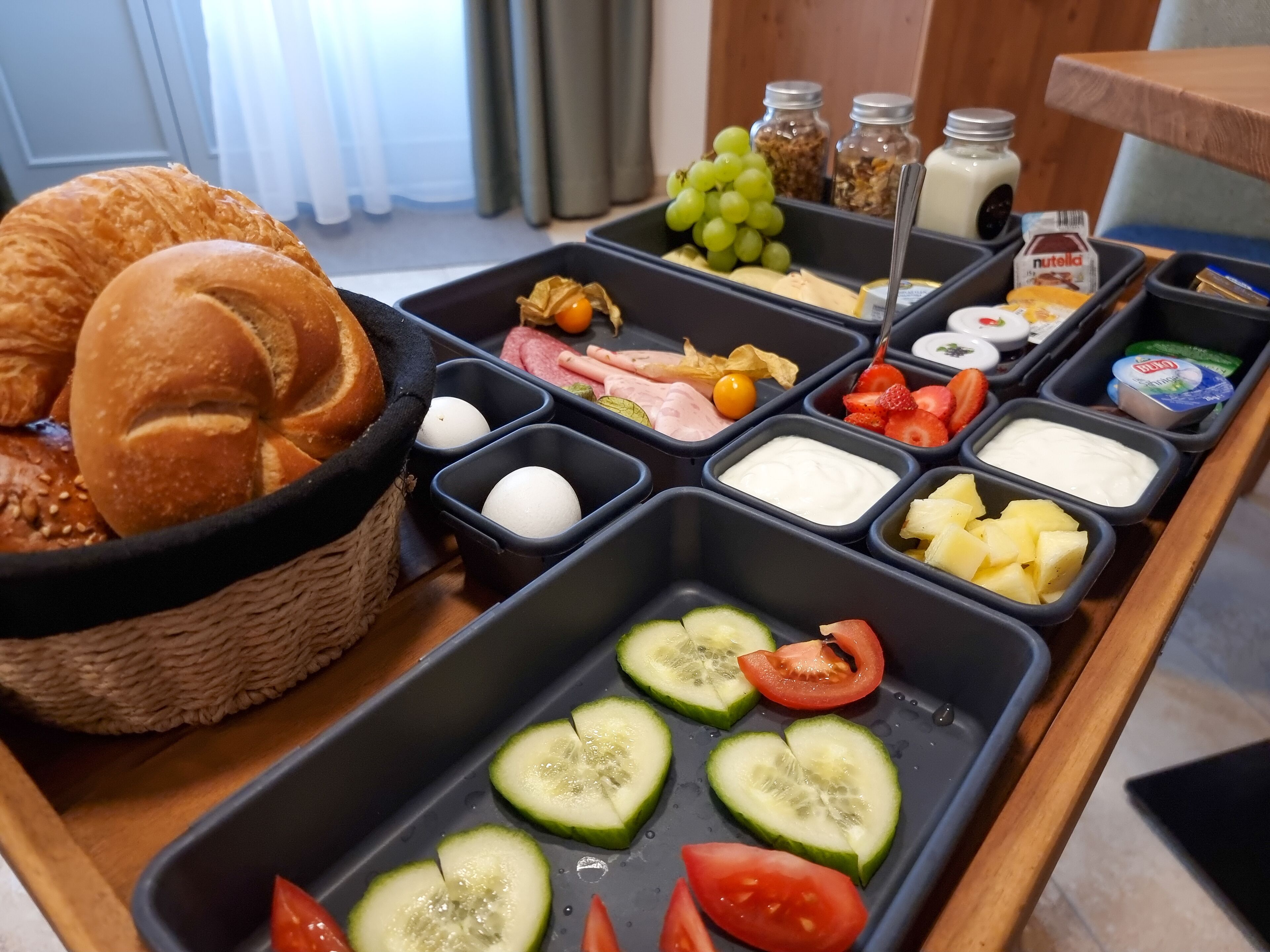 A breakfast buffet with various food items including bread, fruits, cheeses, and spreads.