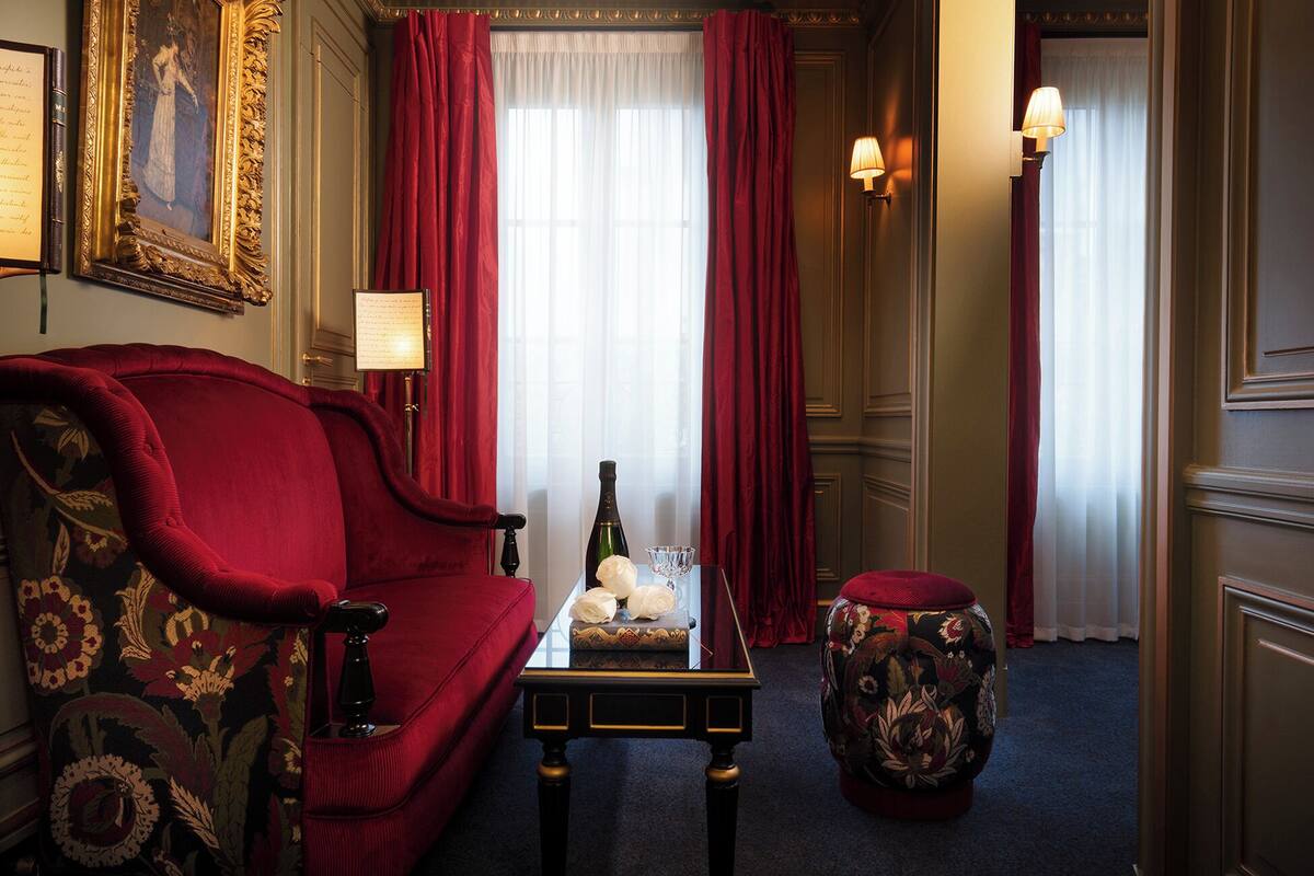 A room with a red sofa, a small table with a bottle and glass, a decorative stool, and a painting on the wall.