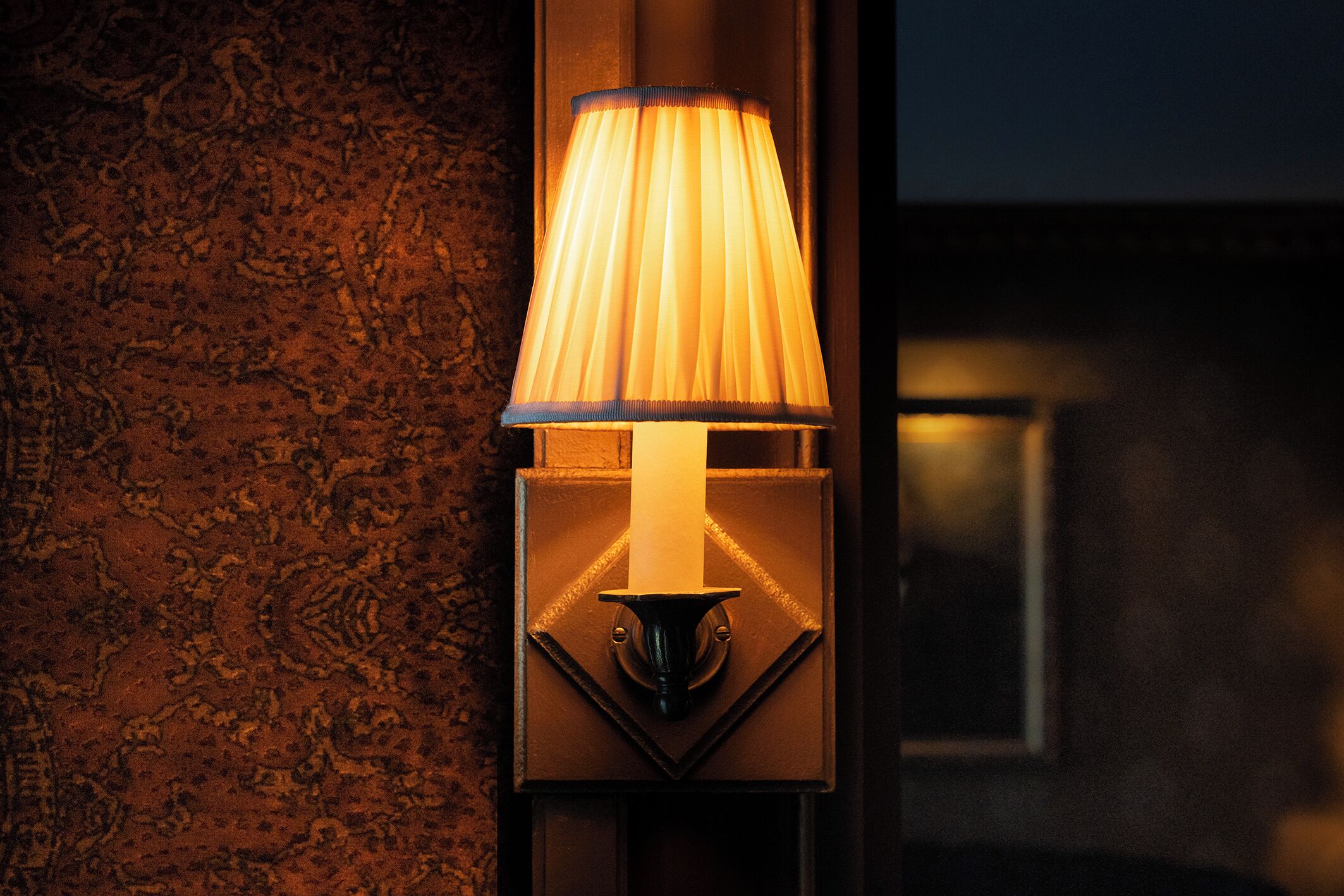 A wall-mounted lamp with a pleated shade, a geometric base, and a textured wall backdrop.