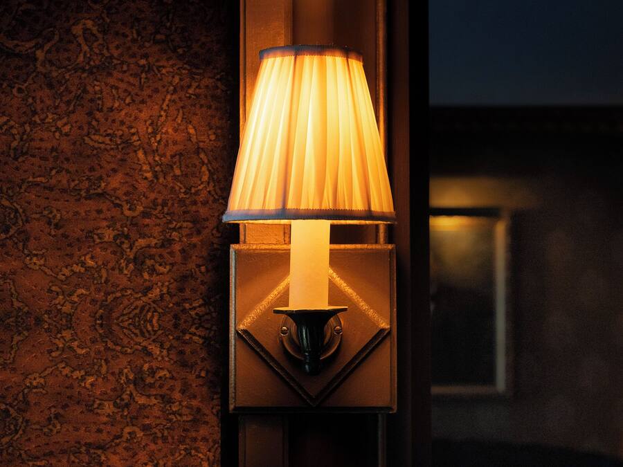 A wall-mounted lamp with a pleated shade, a geometric base, and a textured wall backdrop.