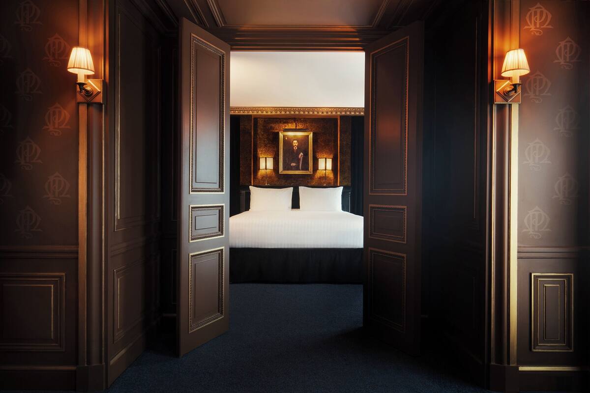 A hotel room with a bed, two wall-mounted lamps, a framed picture above the bed, and dark wood paneling.