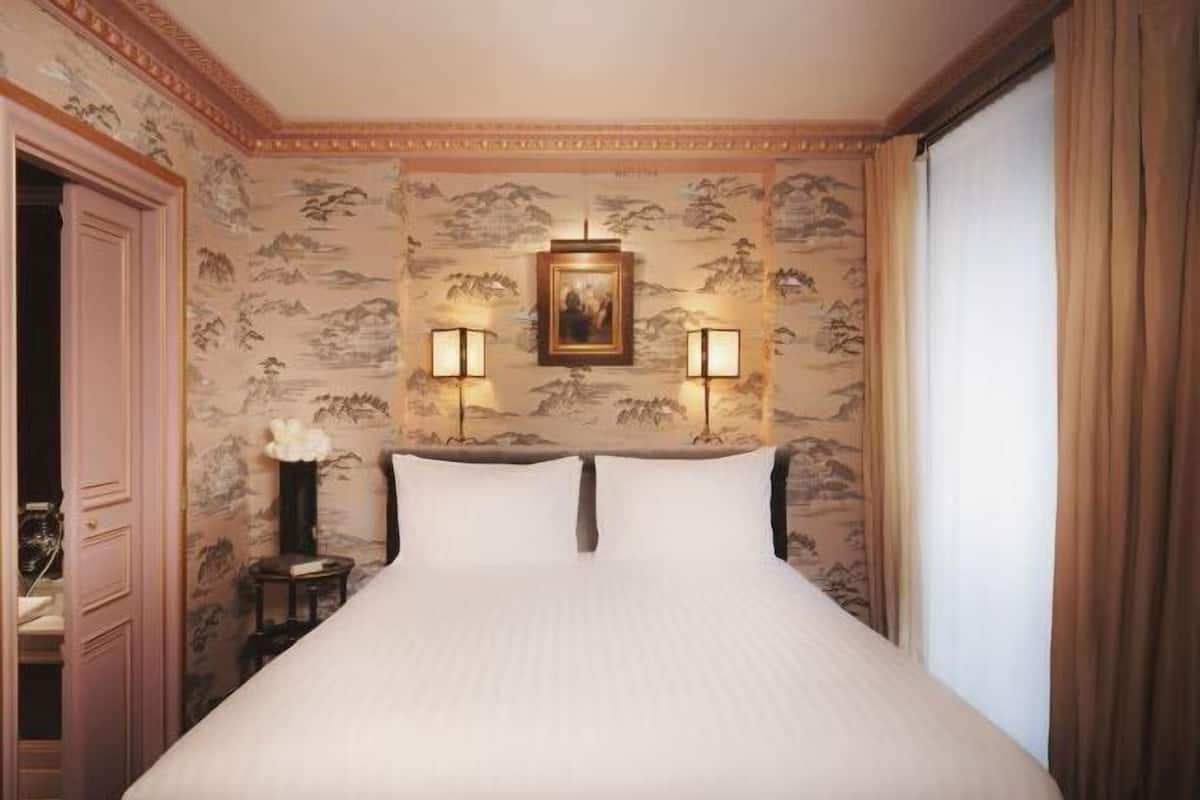 Ein Hotelzimmer mit einem großen Bett, zwei Wandlampen, einem gerahmten Bild über dem Bett und einer Wand mit Bergdekor.
