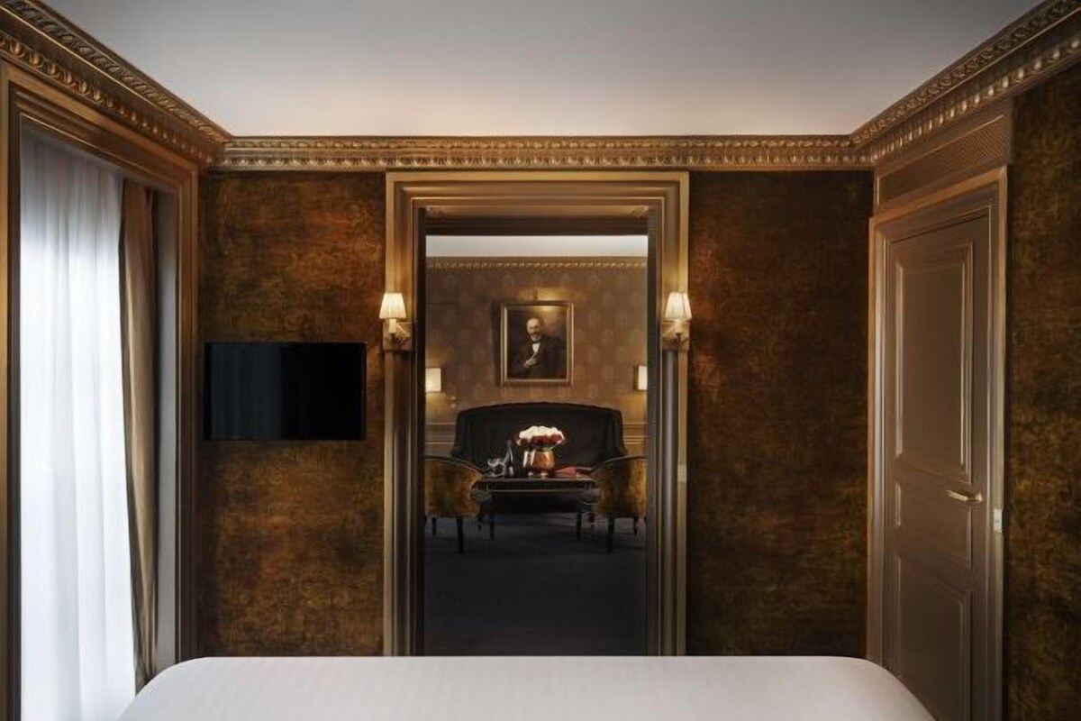 A hotel room with a bed, a desk, a chair, a television, and a framed picture on the wall.