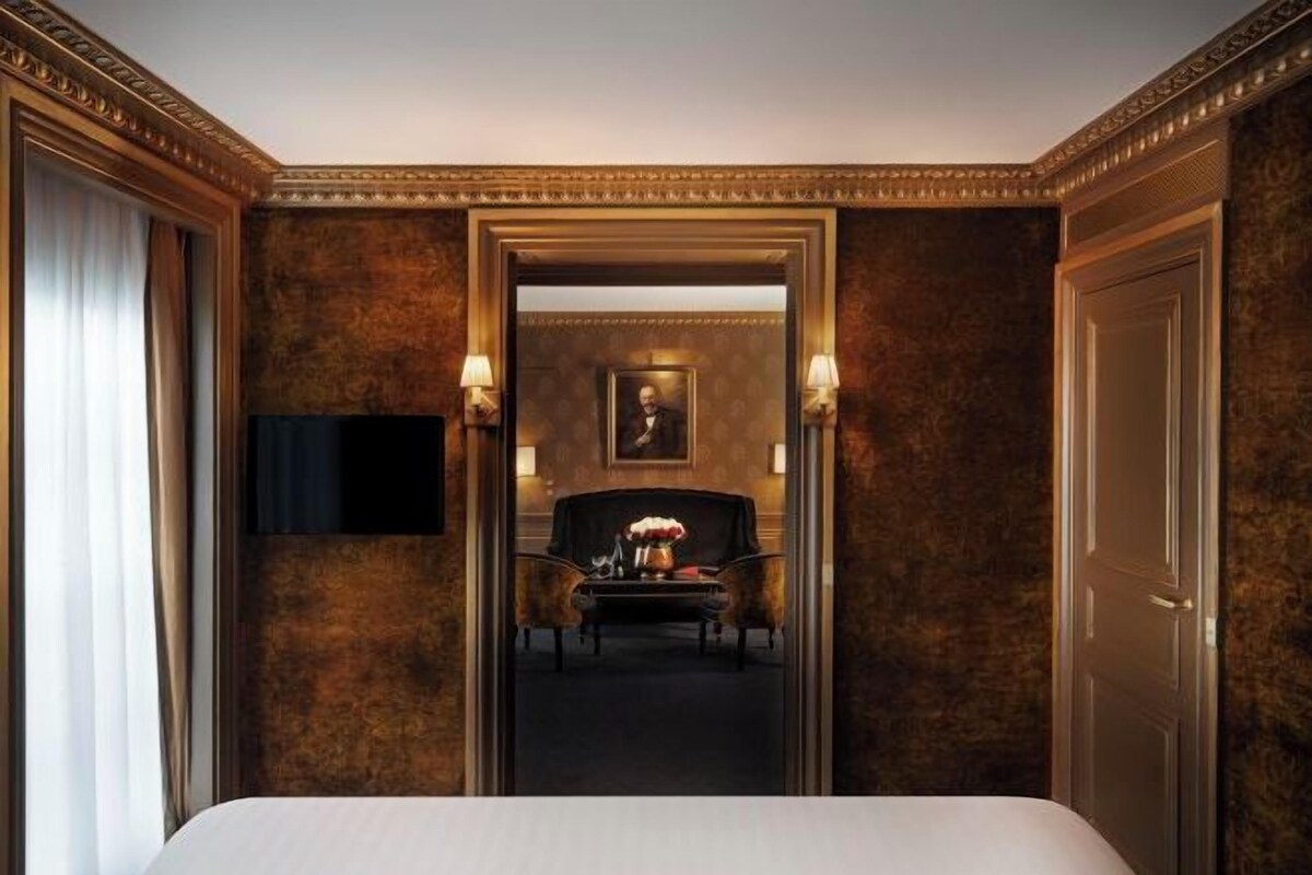 A hotel room with a bed, a desk, a chair, a television, and a framed picture on the wall.