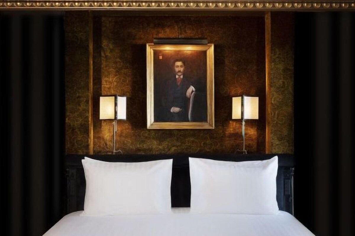 A hotel room with a large bed, two bedside lamps, and a framed portrait on the wall.