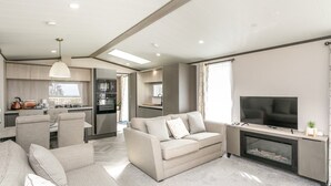 A modern living room with a sofa, TV, fireplace, and kitchen area. - 2 bedroom accommodation in Wigton (Wigton)