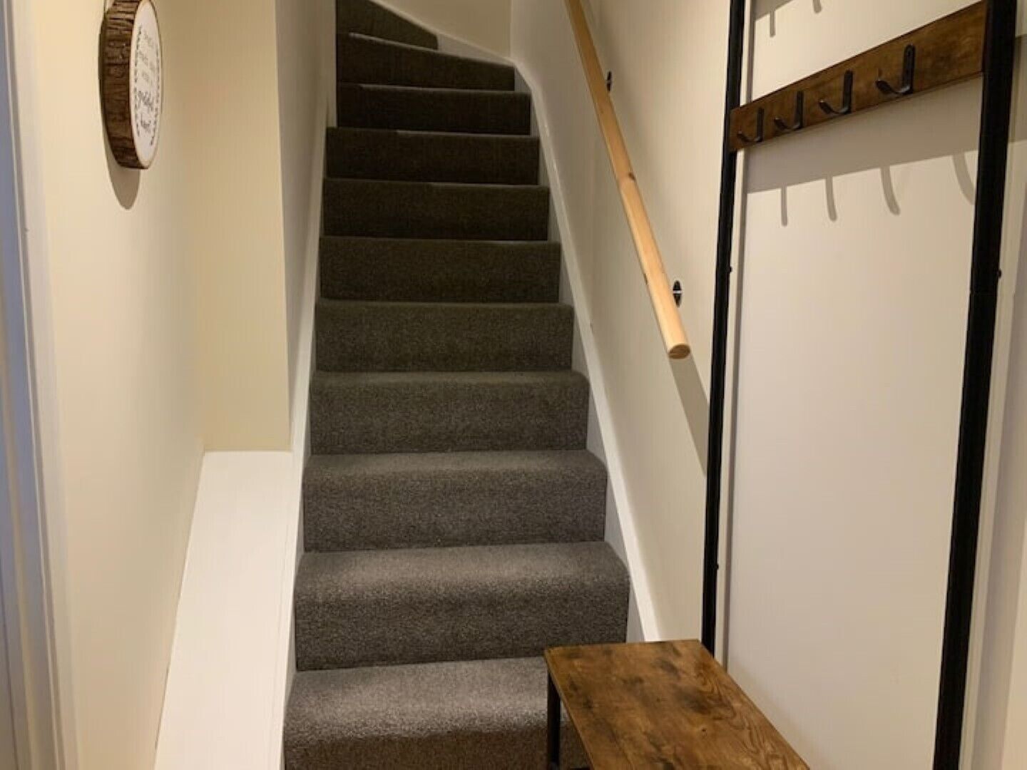 A staircase with carpeted steps leading to a door with a coat rack.
