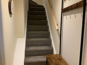 A staircase with carpeted steps leading to a door with a coat rack.