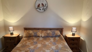 Un dormitorio con una cama, dos mesitas de noche, una lámpara sobre cada una y un reloj de pared, además de una toalla sobre la cama.
