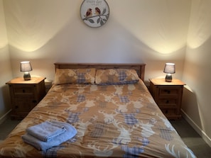A bedroom with a bed, two bedside tables, a lamp on each table, a wall clock, and a towel on the bed.