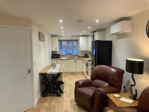 A compact living space with a dining area, a leather chair, a small table, and a kitchen in the background.