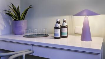 Eine weiße Arbeitsplatte mit einem Blumentopf, zwei Flaschen Mineralwasser und einer violetten Lampe.