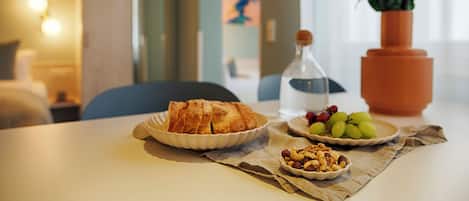A breakfast table with croissants, grapes, and nuts, a vase of flowers, and a water bottle.