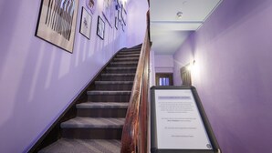 A staircase with a wooden handrail, flanked by purple walls and framed artwork. - homie hotel kunterbunt (Würzburg)