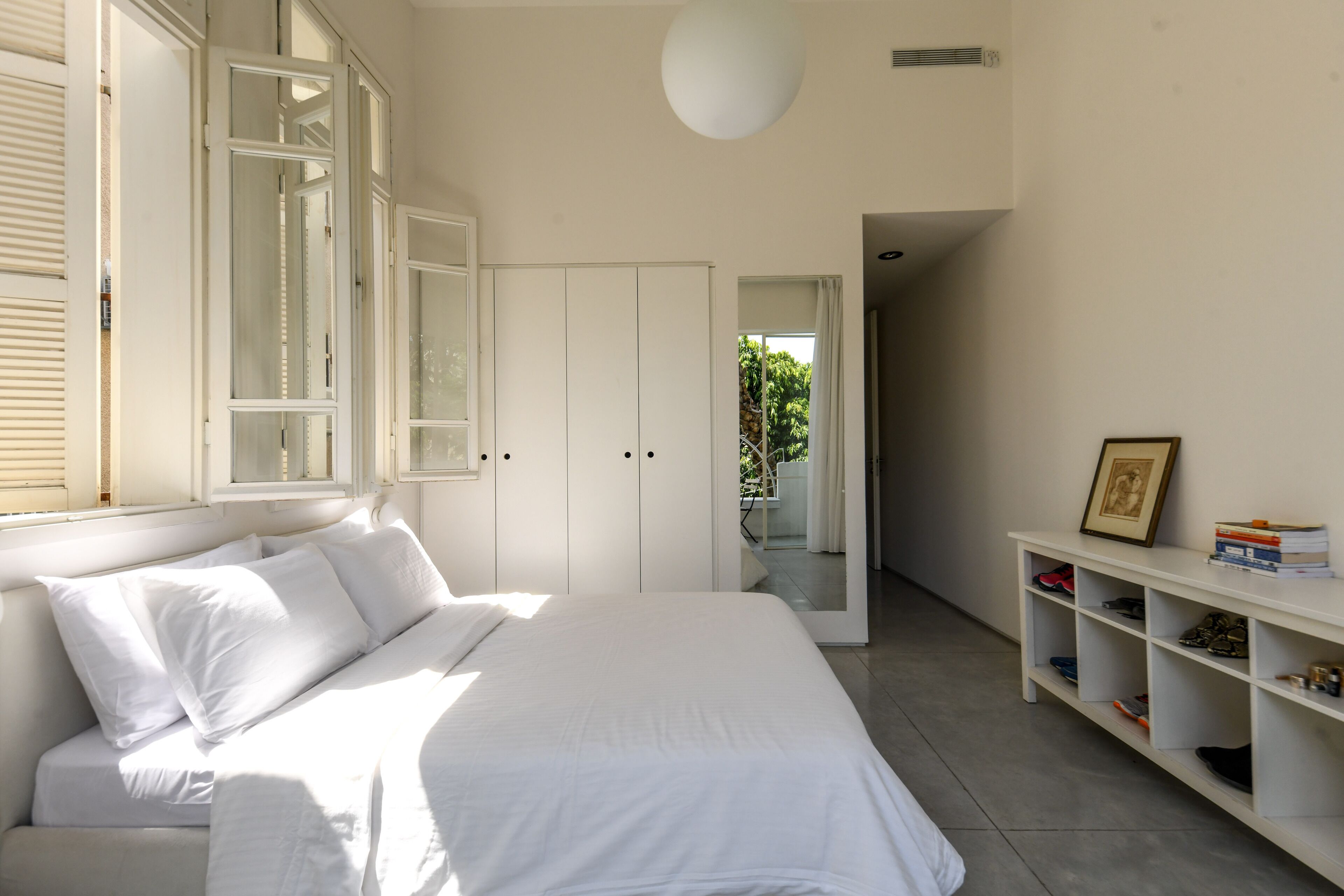 Un dormitorio con cama, armario, zapatero y puerta que da a un balcón.