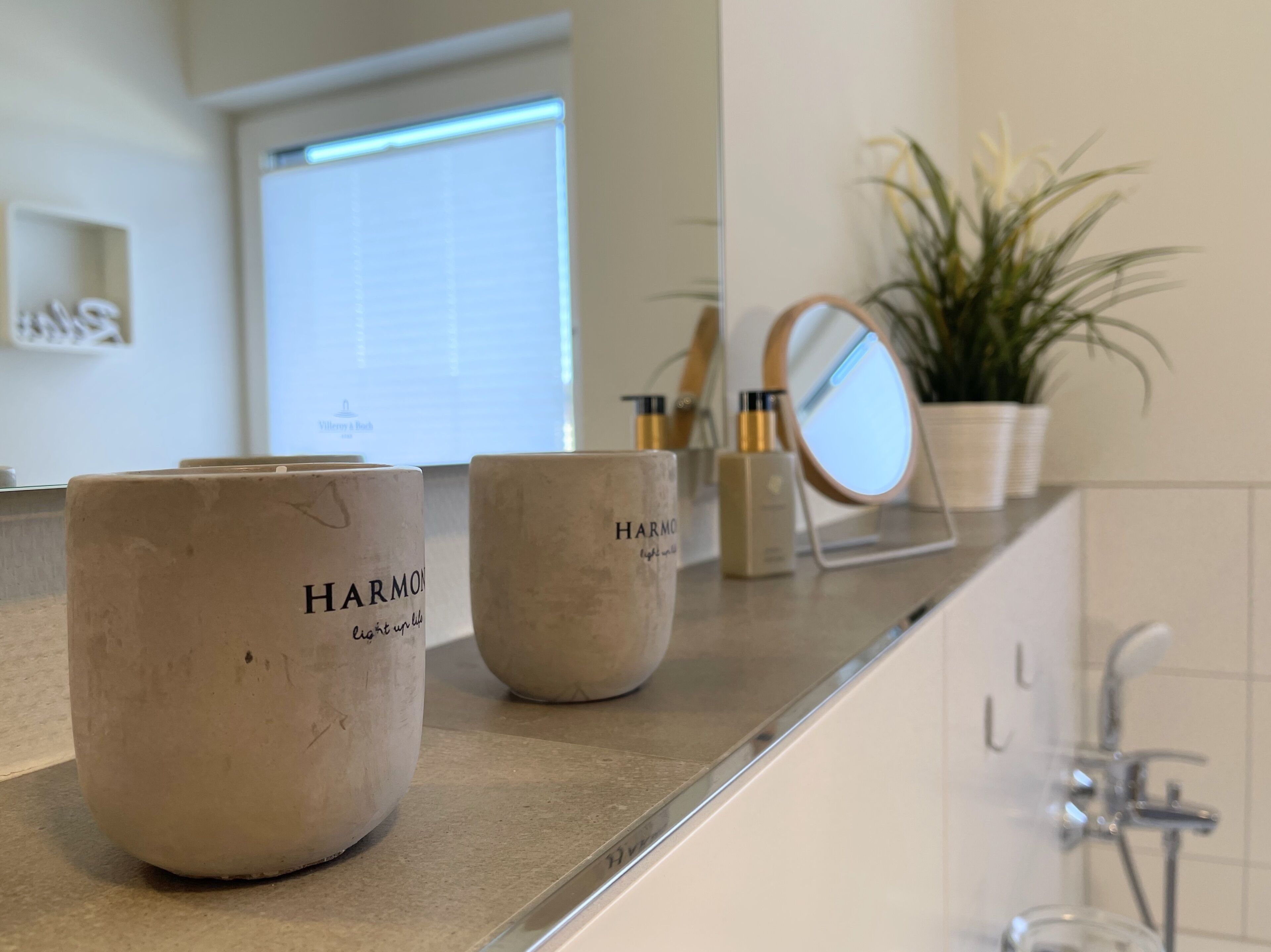 Una encimera de baño con dos frascos de cerámica que dicen "HARMON" y un espejo pequeño.