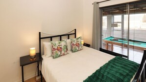 Uma cama com manta verde, duas luminárias laterais e uma janela com persianas.