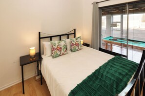 A bed with a green blanket, two bedside lamps, and a window with blinds.