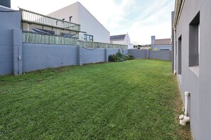Quintal residencial com gramado bem cuidado, cerca de madeira e casa moderna com telhado inclinado.