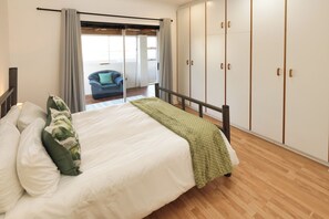 Quarto com cama, manta verde e vista para uma varanda com cadeira.