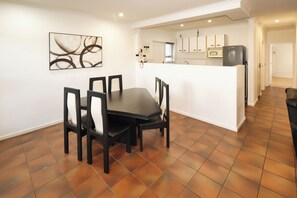 A dining area with a table and chairs, a kitchen in the background, and a tiled floor.