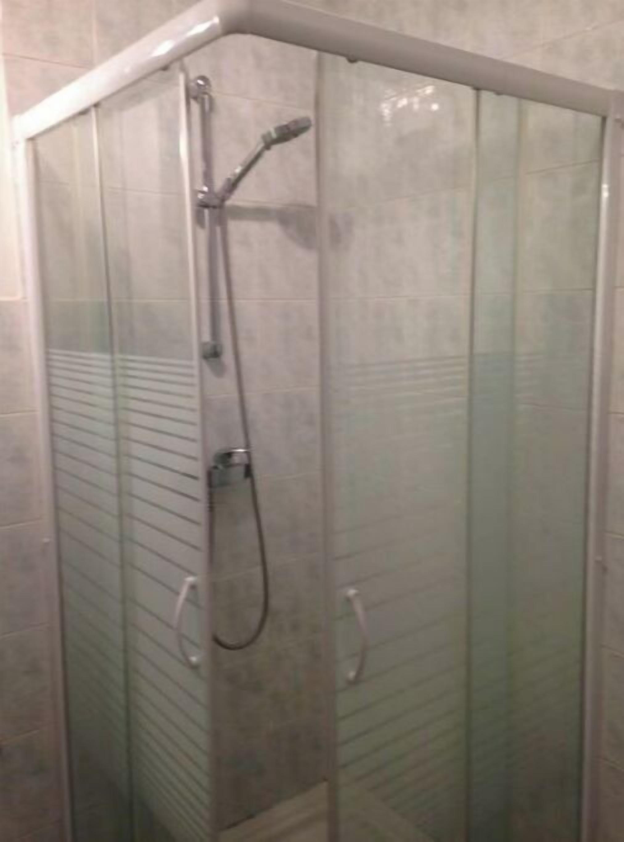 Une cabine de douche fermée par des parois en verre, équipée d’un pommeau de douche à main et d’un robinet à main.