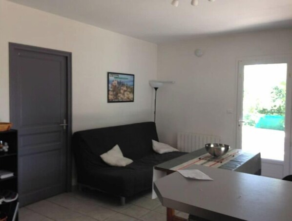 A room with a black sofa, a dining table, a radiator, and a door. - Villa with swimming pool South Ardéche (Lavilledieu)