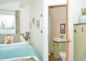Un dormitorio con cama, mesita de noche, lámpara y ventana con cortinas.