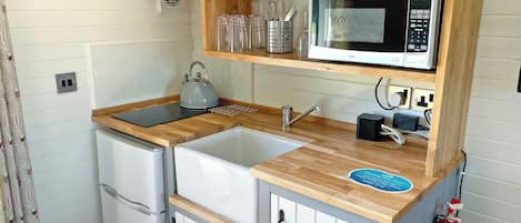 A compact kitchen with a sink, a kettle, a microwave, and a refrigerator.