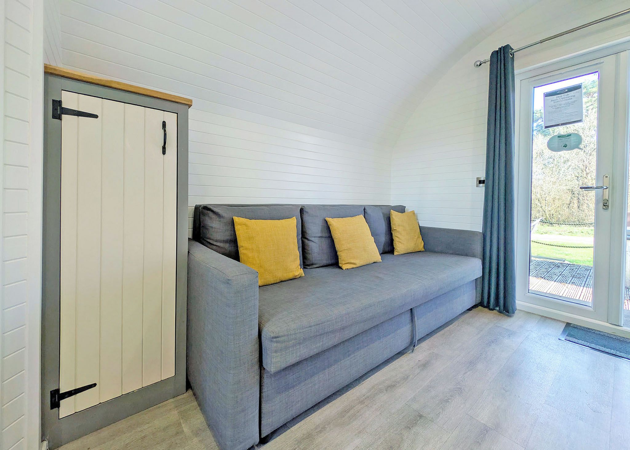 A room with a grey sofa, two yellow cushions, a white wardrobe, and a glass door leading outside.