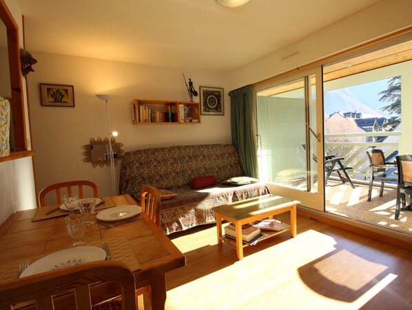Una sala de estar acogedora con una mesa de comedor de madera, un sofá y un balcón con sillas.