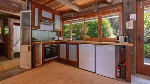 A compact kitchen with wooden cabinets, a built-in oven, a dishwasher, and a window overlooking greenery. - Chill Out - couples retreat on the lake - short drive to Seal Rocks (Bungwahl)