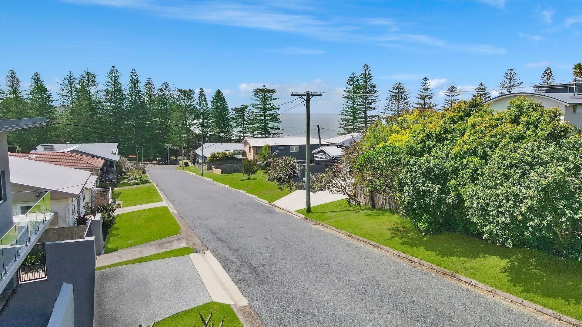 A residential street with houses, a clear sky, and greenery.