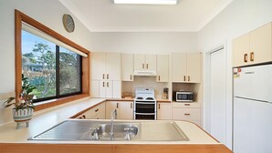 Une cuisine moderne avec des meubles blancs, un évier en acier inoxydable, une cuisinière, un four à micro-ondes et un réfrigérateur.