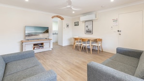 Een moderne woonkamer met een flatscreen televisie, een houten eettafel met stoelen en grijze banken.