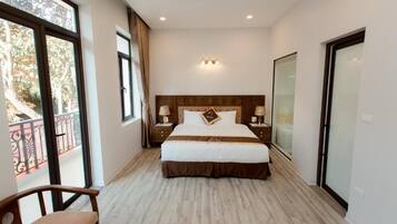 A hotel room with a large bed, two bedside tables, a chair, and a balcony with a railing.