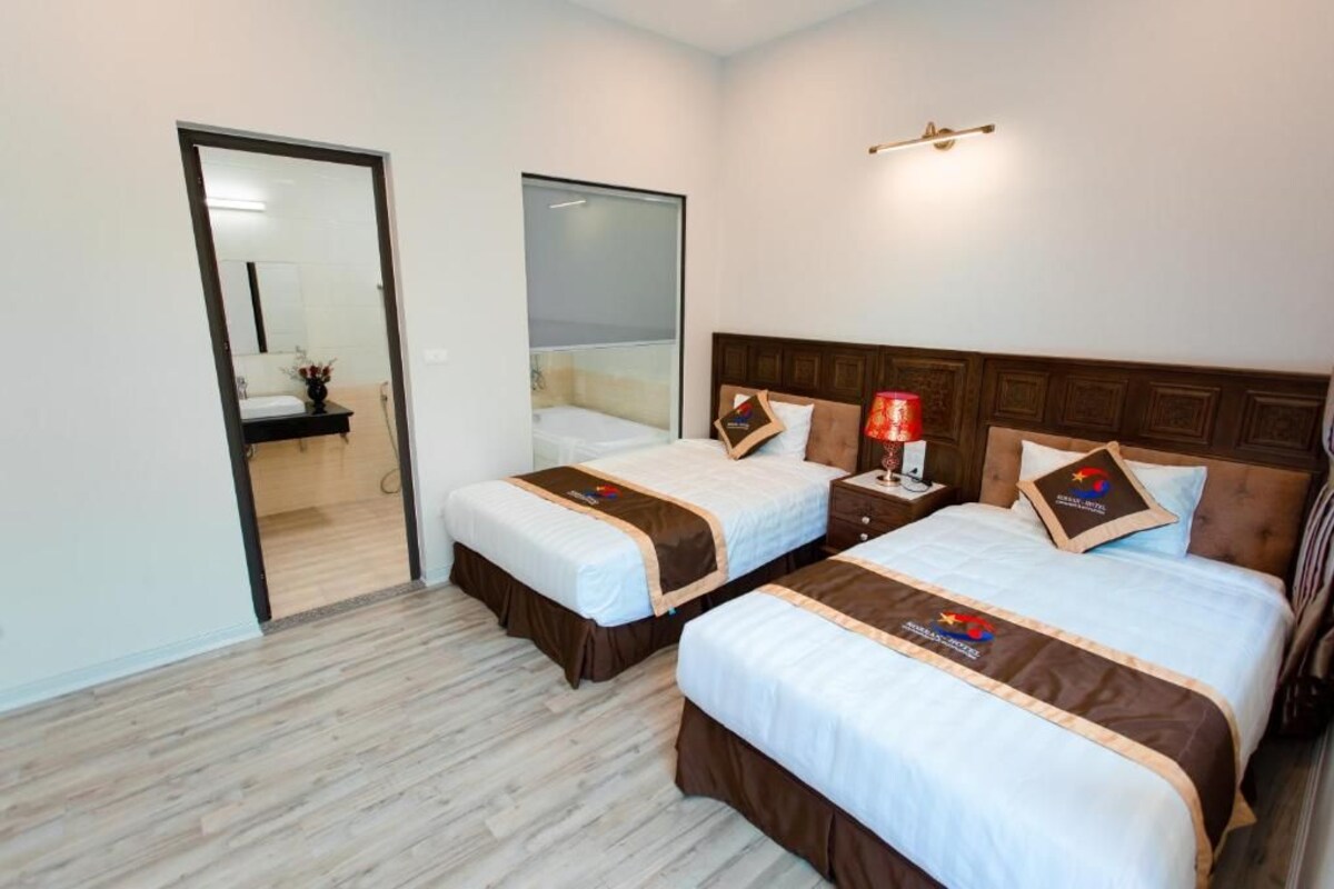 Een hotelkamer met twee bedden, een nachtkastje, een spiegel en een deur naar een andere kamer.