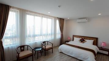 A hotel room with a large bed, two chairs, a small table, and a nightstand with a lamp.