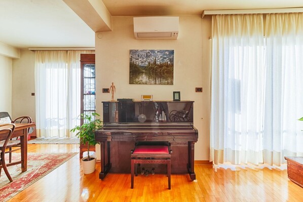 Un salon avec un piano, un coin repas avec des chaises, une plante en pot et un tableau accroché au mur.