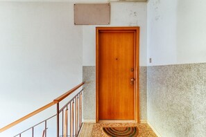 Une porte en bois avec un bouton de porte et une poignée en métal, une rambarde en bois et un paillasson texturé.