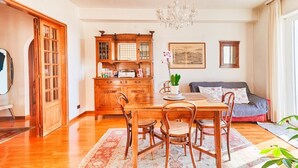 Un coin repas avec une table et des chaises en bois, un lustre et un canapé avec des coussins.