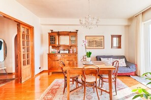 Un coin repas avec une table et des chaises en bois, un lustre et un canapé avec des coussins.