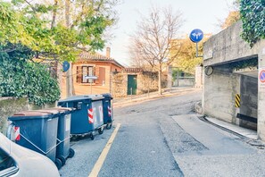 Een straat met vuilcontainers, een gebouw met een pannendak, en een blauw verkeersbord.