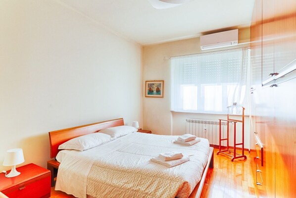 Une chambre d’hôtel avec un lit, une table de chevet, une fenêtre avec des stores et un radiateur.
