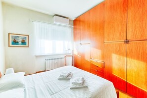 Een hotelkamer met een bed, een houten garderobe, een radiator en een raam met gordijnen.