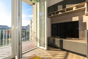 Ein Balkon mit einer Schiebetür, einem flachbildfernseher an einer Holzkommode und Blick auf die Stadtlandschaft.