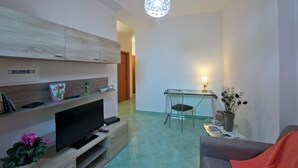 Ein modernes Wohnzimmer mit Flachbildfernseher, Essbereich mit Tisch und Stühlen und einer dekorativen Pendelleuchte.