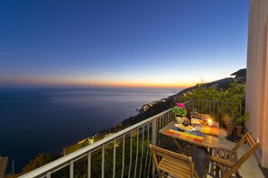 A balcony with a table set for dining, overlooking a coastal view during sunset. - Emerald apartment with stunning panoramic sea view Amalfi Coast (Furore)