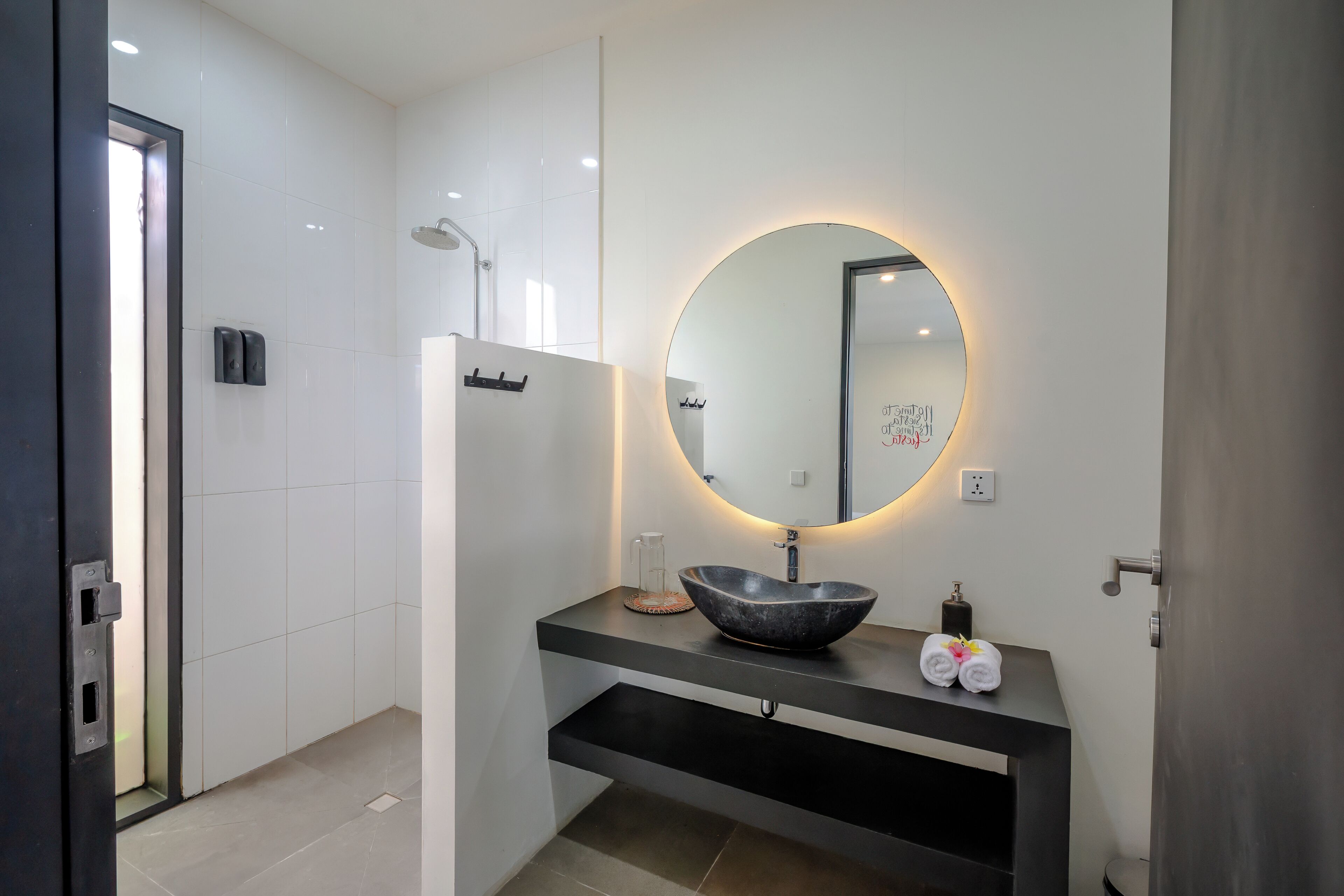 A modern bathroom with a round mirror, a black sink, and a shower.