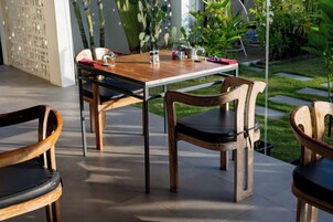 Un área de comedor al aire libre con una mesa y sillas de madera, una planta en maceta y un cactus al fondo.